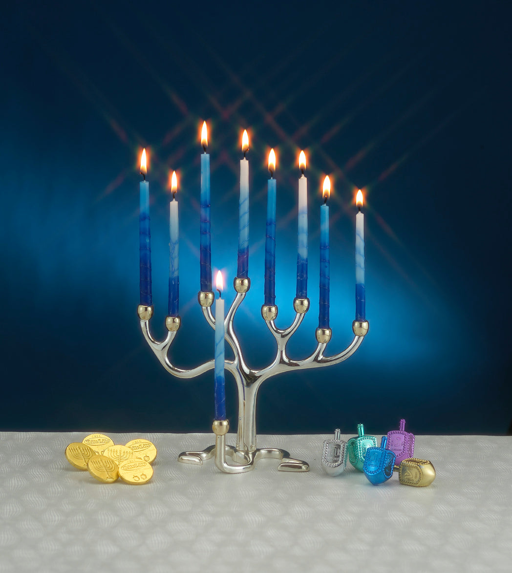 A medium sized, silver plate finish and gold tone cups tree of life menorah with candles lit, next to dreidels and coins