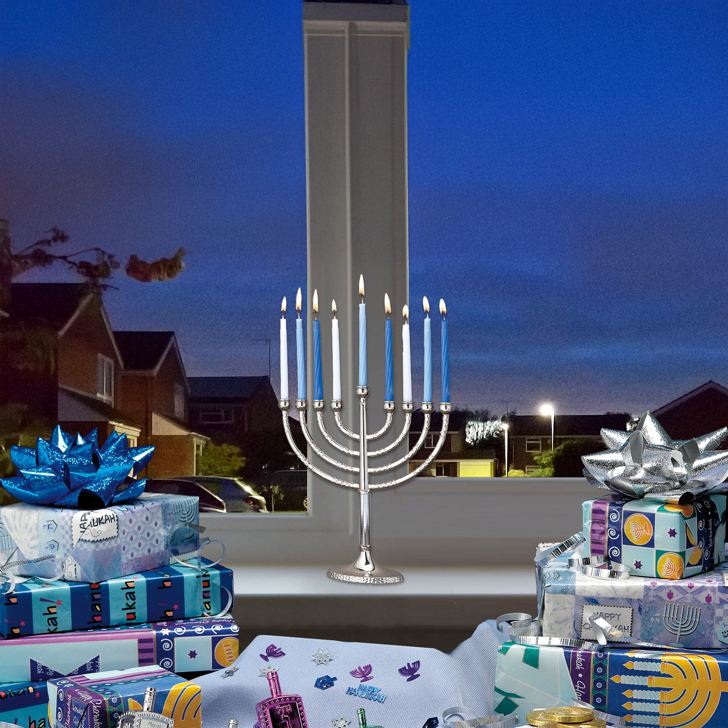A nickel plated menorah with candles lit displayed in a window