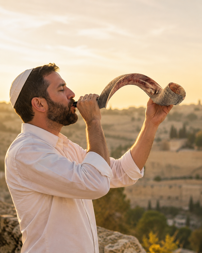 Man blowing a large half-polished Yemenite shofar at sunset overlooking Jerusalem