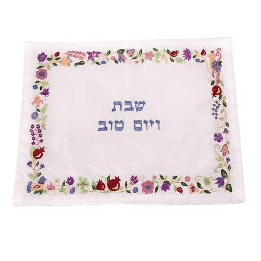 Challah cover with an embroidered border of pomegranates and flowers and blue Hebrew letters in the center