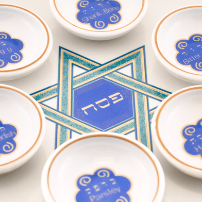 White seder plate with copper color around the border and a green and blue Star of David in the center