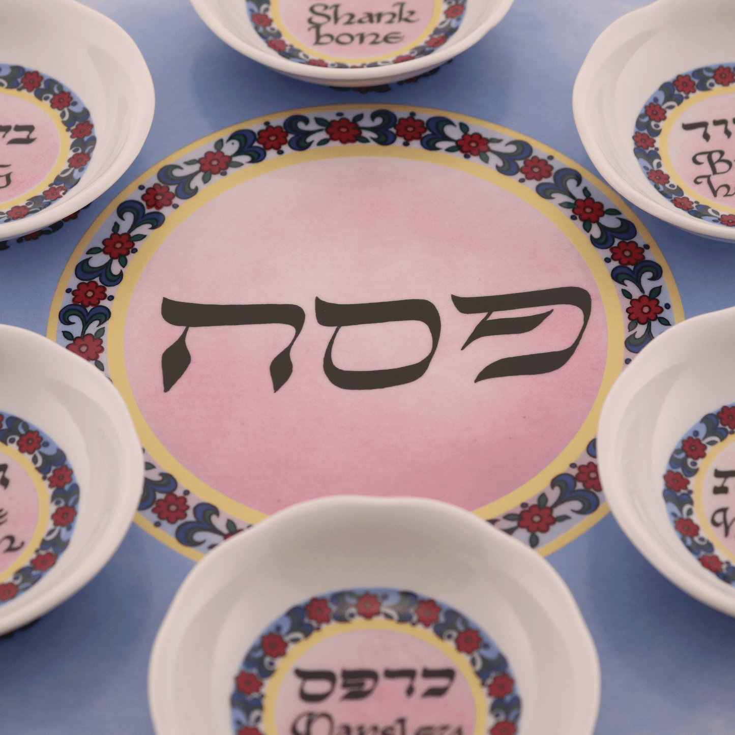 Pink and blue seder plate with a floral design and green trim around the edges