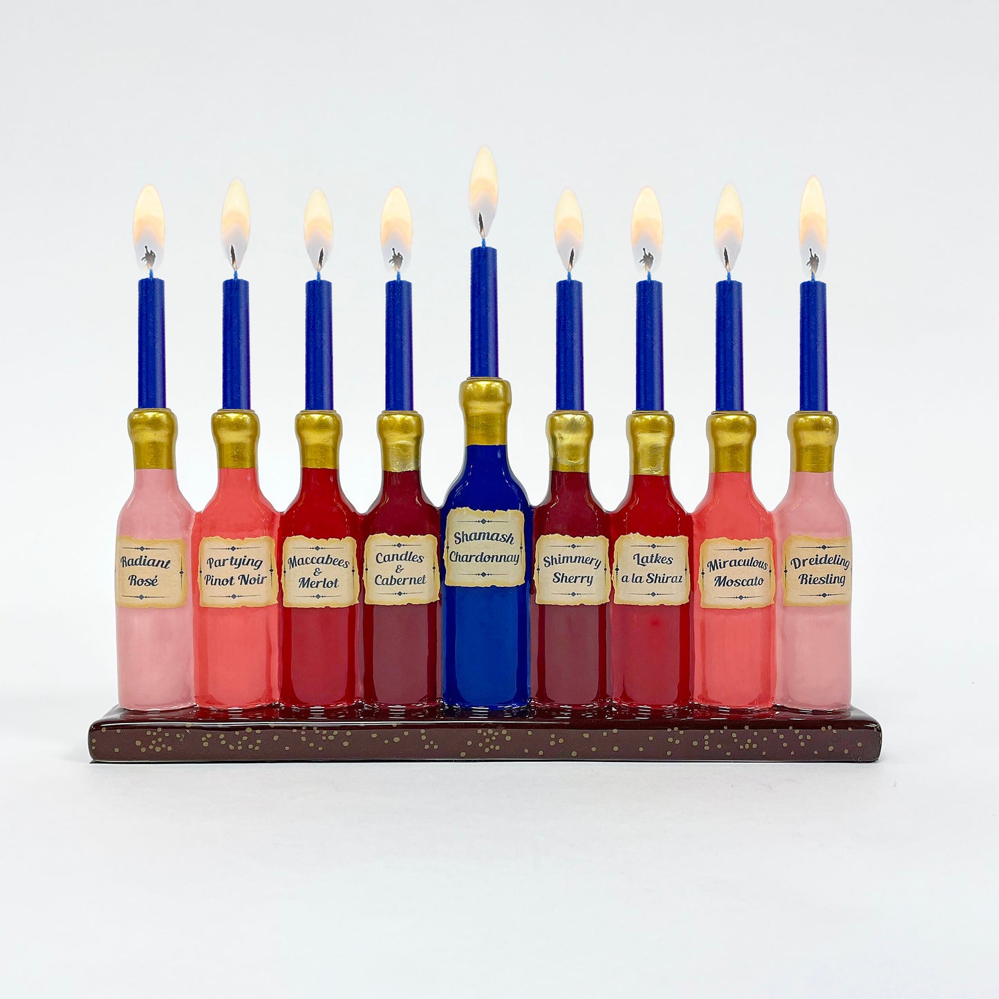 A hand-painted ceramic menorah designed to look like fine wine bottles, featuring gold accents and holiday-themed names on the bottles.