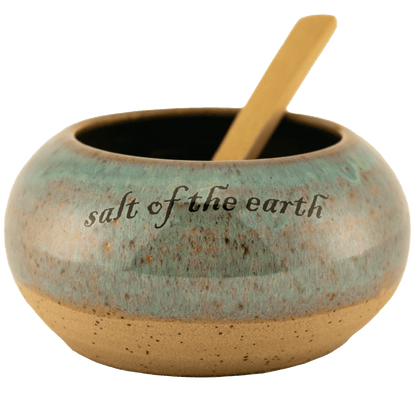 Deep teal ceramic salt bowl that says "salt of the earth" in English and Hebrew with a wooden spoon