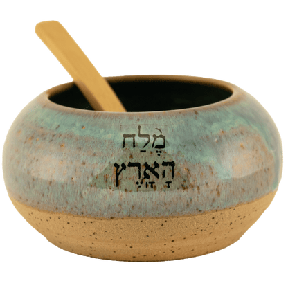 Deep teal ceramic salt bowl that says "salt of the earth" in English and Hebrew with a wooden spoon