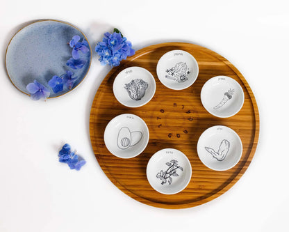 Bamboo Passover Seder plate with porcelain bowls featuring black and white illustrations next to blue flowers