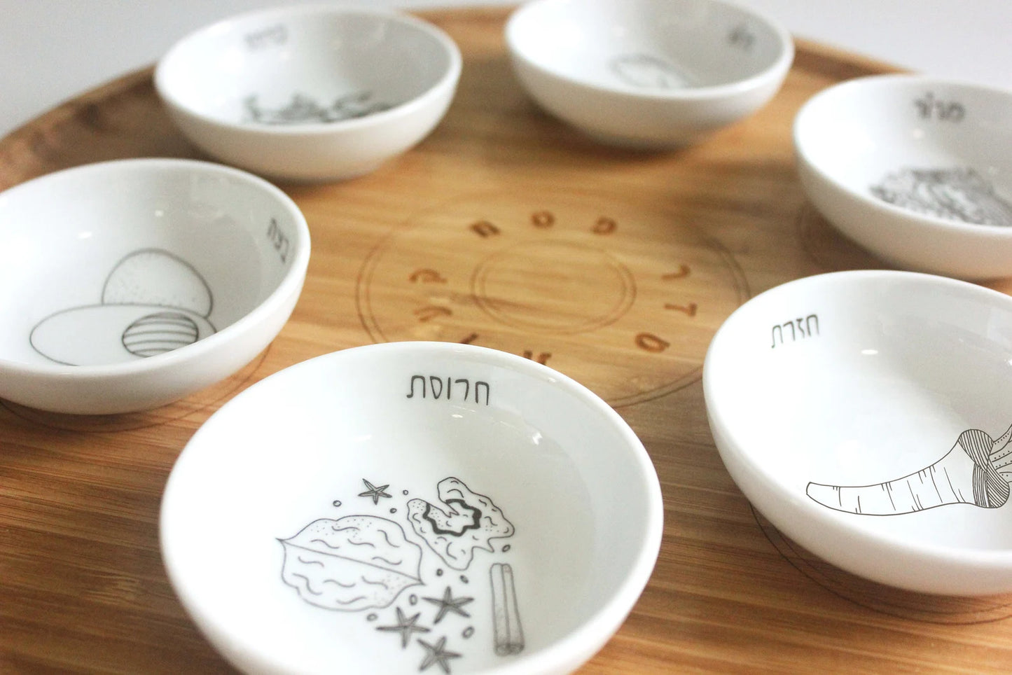 Closeup angle of Bamboo Passover Seder plate with porcelain bowls featuring black and white illustrations 