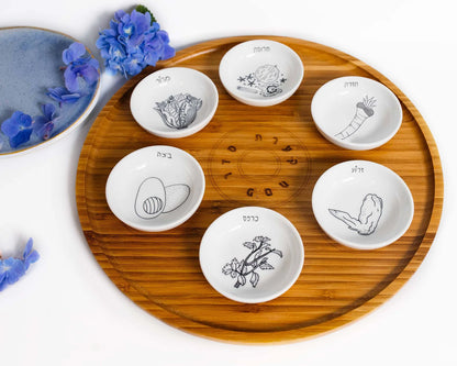 Closeup of Bamboo Passover Seder plate with porcelain bowls featuring black and white illustrations next to blue flowers