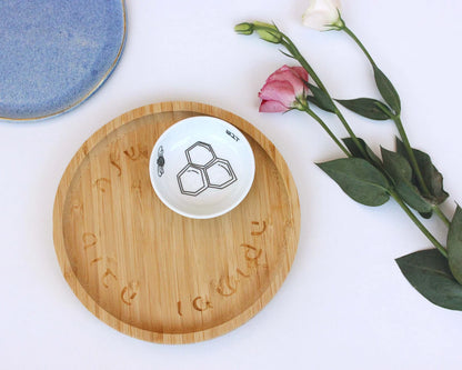 Porcelain bowl with a delicate black and white illustration of a bee and honey and a bamboo tray next to roses
