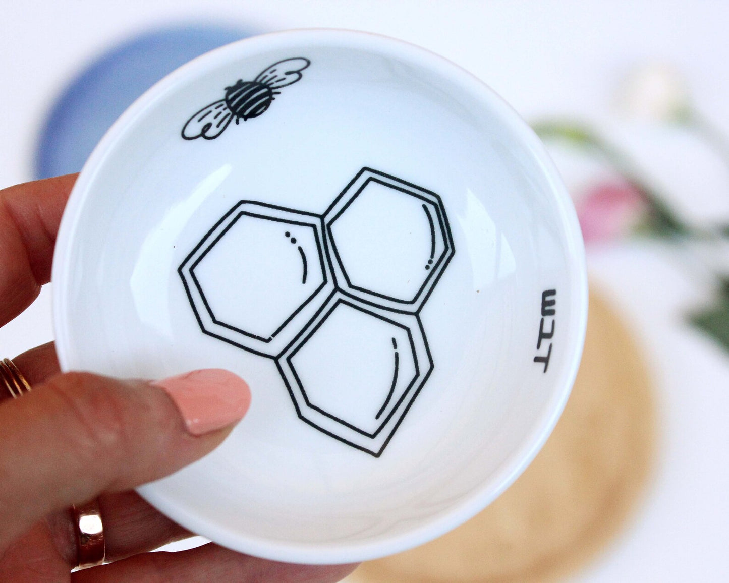 Hand holding porcelain bowl with a delicate black and white illustration of a bee and honey