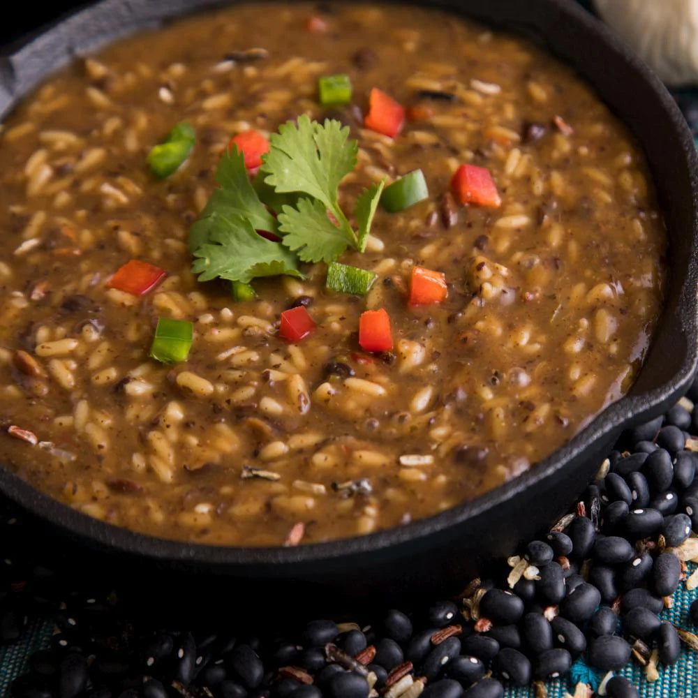 black bean soup with cilantro and diced peppers on top in black skillet 