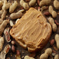 peanut butter spread over piece of bread with open shell and whole peanuts all around