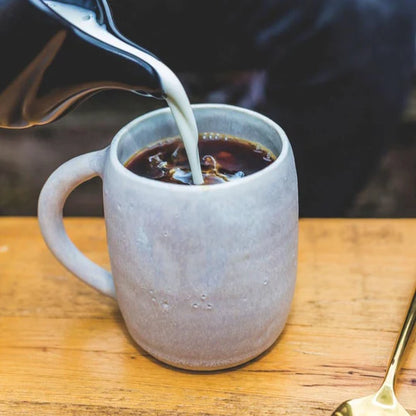 ready hour creamer being poured from black dish into grey coffee cup with gold spoon on right side of cup