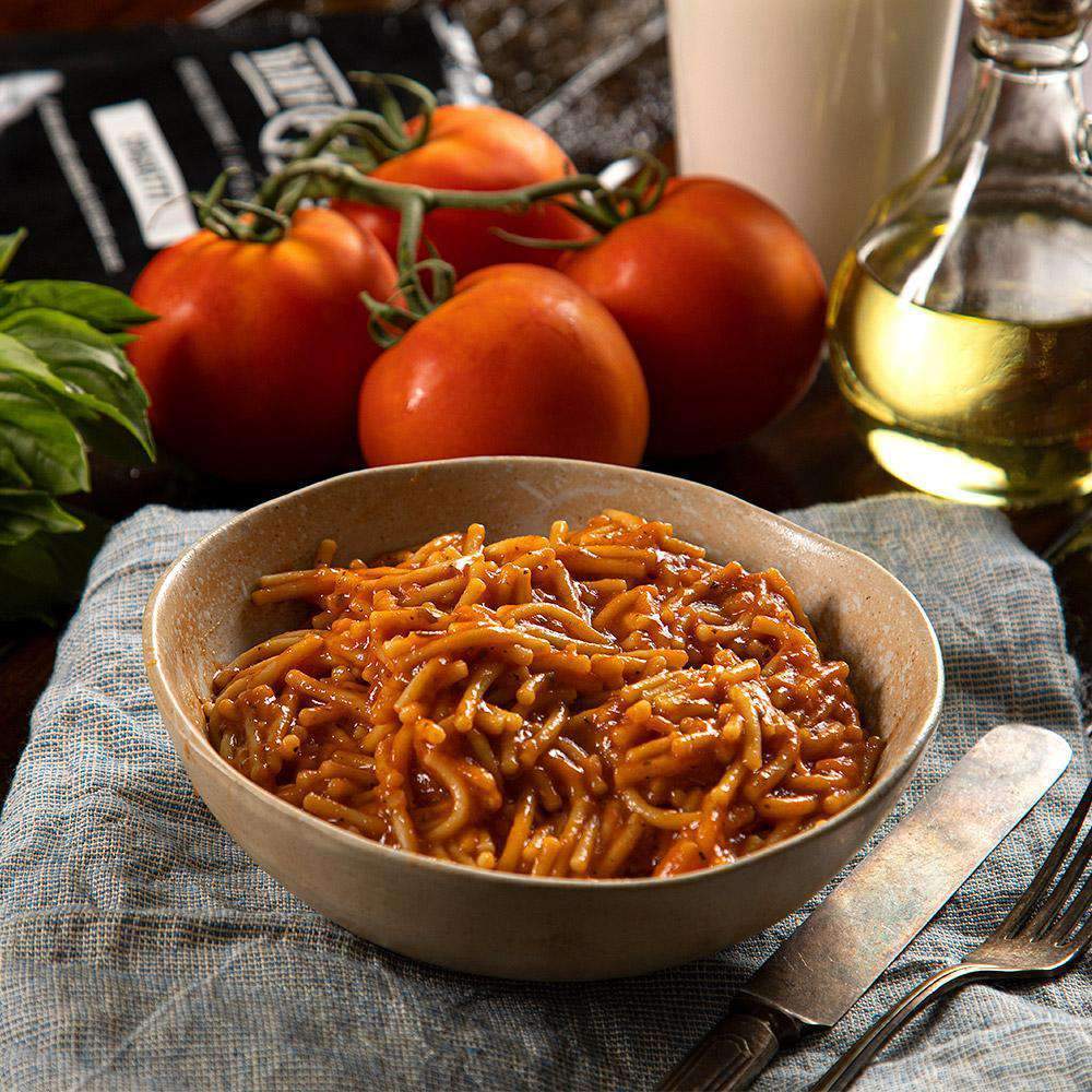 spaghetti with red sauce in bowl with cutlery on right side 