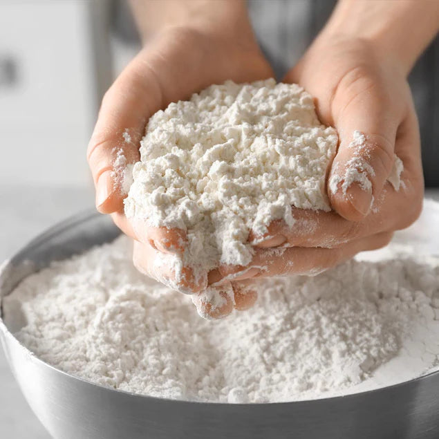 two hands holding flour over a big silver bowl of flour 