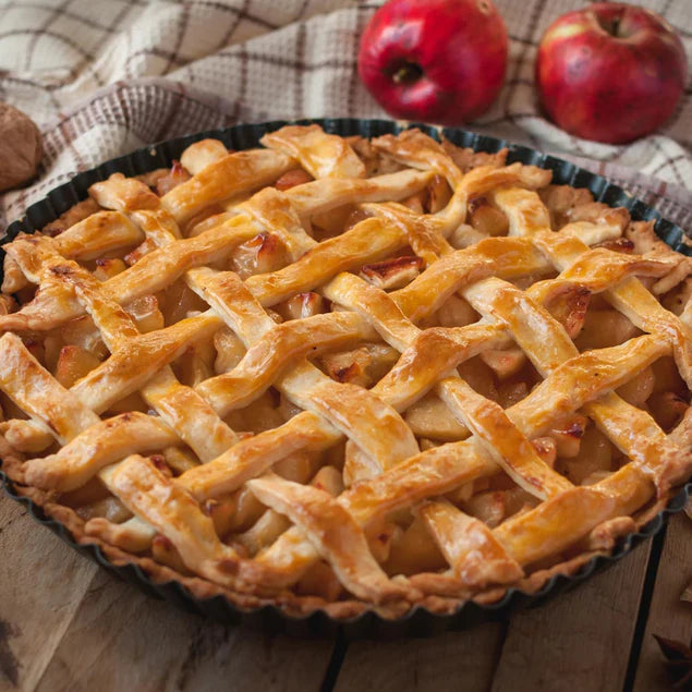 apple pie in large dish with two apples on the right side of the pie 