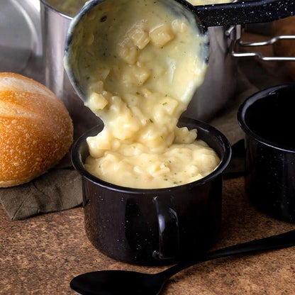 homestyle potato soup being ladled into black dish with bread in background and black spoon in front of dish