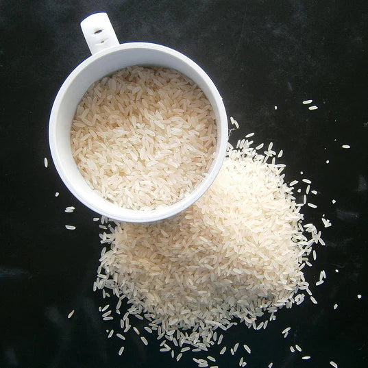 white cup halfway full of uncooked long grain white rice with pile of long grain white rice next to it