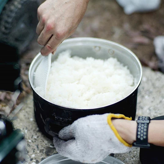 cooked long grain white rice being stirred by person with one glove on in black pot