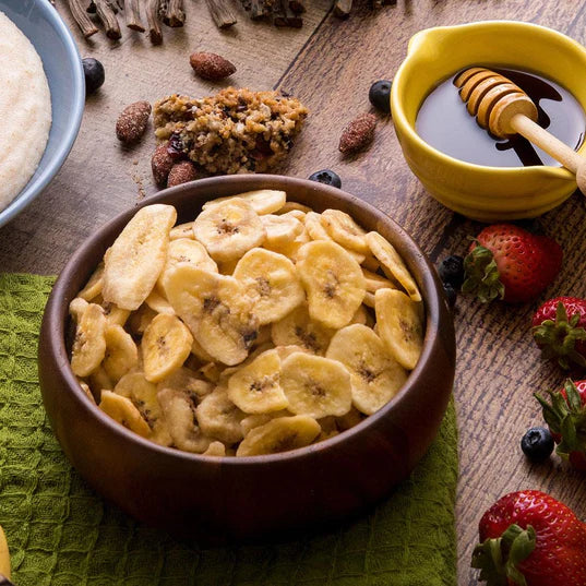 banana chips in wooden bowl with strawberries honey and nuts around bowl 