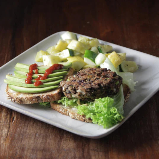 black bean burger patty on whole grain bread with avocado ketchup lettuce and a side of vegetables 