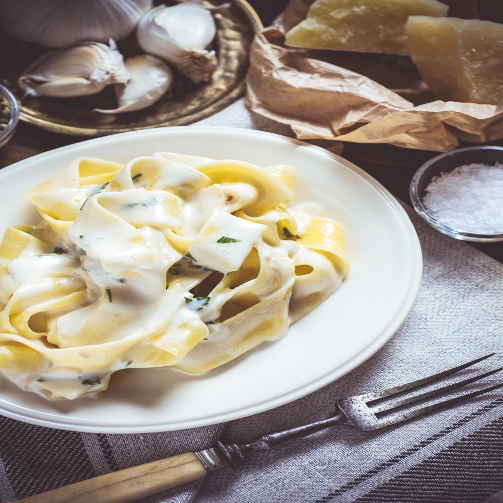 cooked creamy alfredo pasta with white sauce on top on white plate with long fork on the right side 