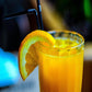 orange energy drink with orange slice on side of glass and black straw in glass