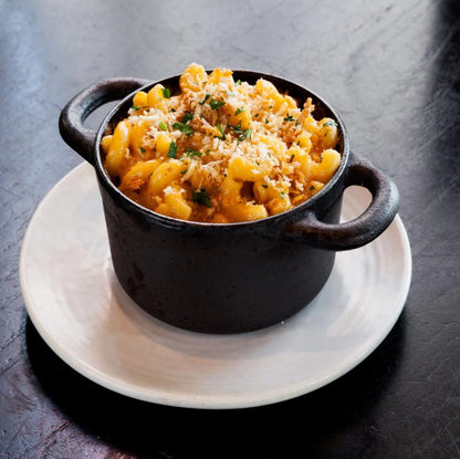 cooked mac and cheese with herbs and bread crumbs on top in black dish