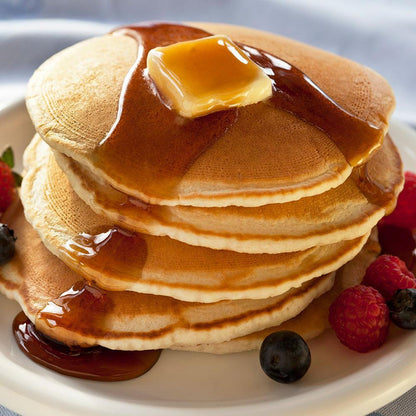 buttermilk pancakes with melting butter and syrup on top and blueberries raspberries and strawberries on white plate