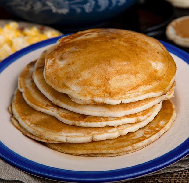 stack of four buttermilk pancakes on white and blue plate with cooking pancakes in the background 