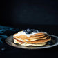 stack of ready hour pancakes with blueberries and melted butter on top on blue plate 
