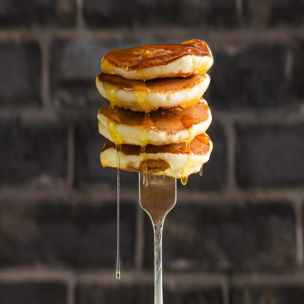 four stacked mini pancakes stuck on fork with syrup dripping down pancakes 